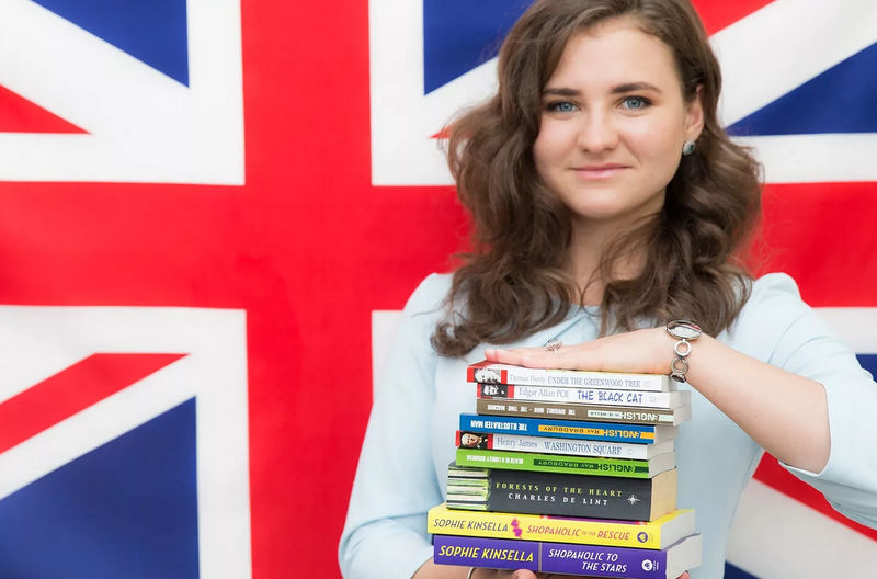 Девушка стоит на фоне английского флага со стопкой книг